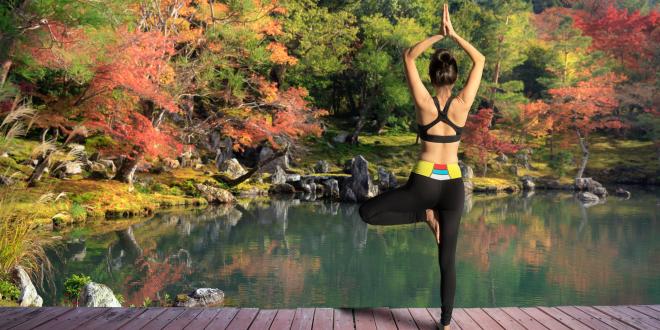 Woman in work out clothes doing tree pose on the dock of a pond during fall. 
