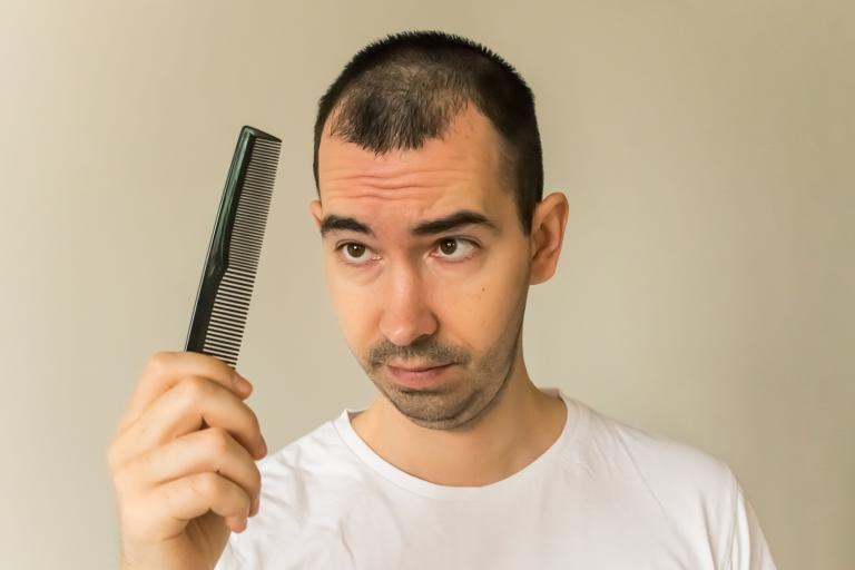 a middle-aged man looking at his comb with worry